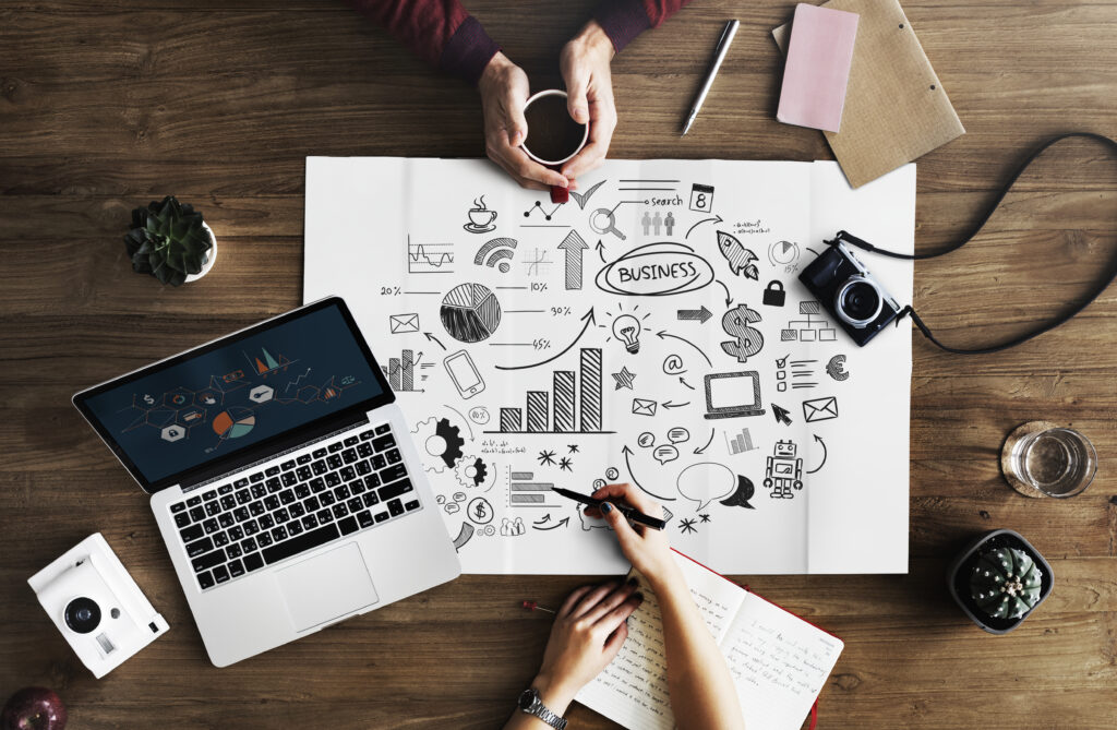 Girl's hand drawing Strategical map for outsource content marketing with cameras, laptop, book and pen on the table