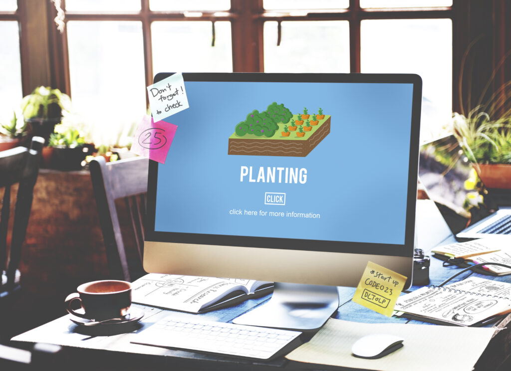 Moniter displaying planting service on the table along with the tea, mouse and papers